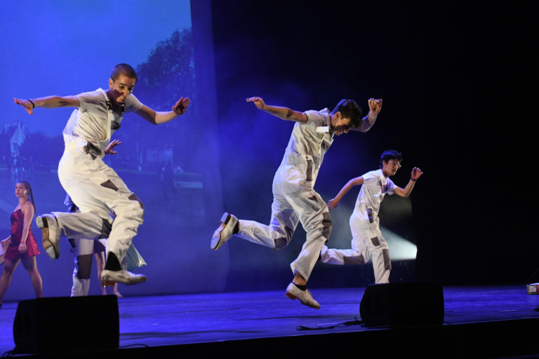 Trois danseurs en plein saut sur scène, lors d'un spectacle